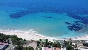An aerial view of a beach with clear blue waters and a sandy shore. There are buildings and greenery in the foreground. - A terrace overlooking the sea 19084041C226886 (Sicilia)
