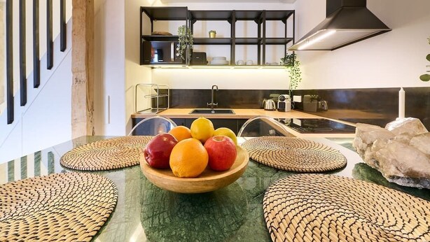 A modern kitchen with a marble countertop, a wooden bowl of fruit, and a black range hood.