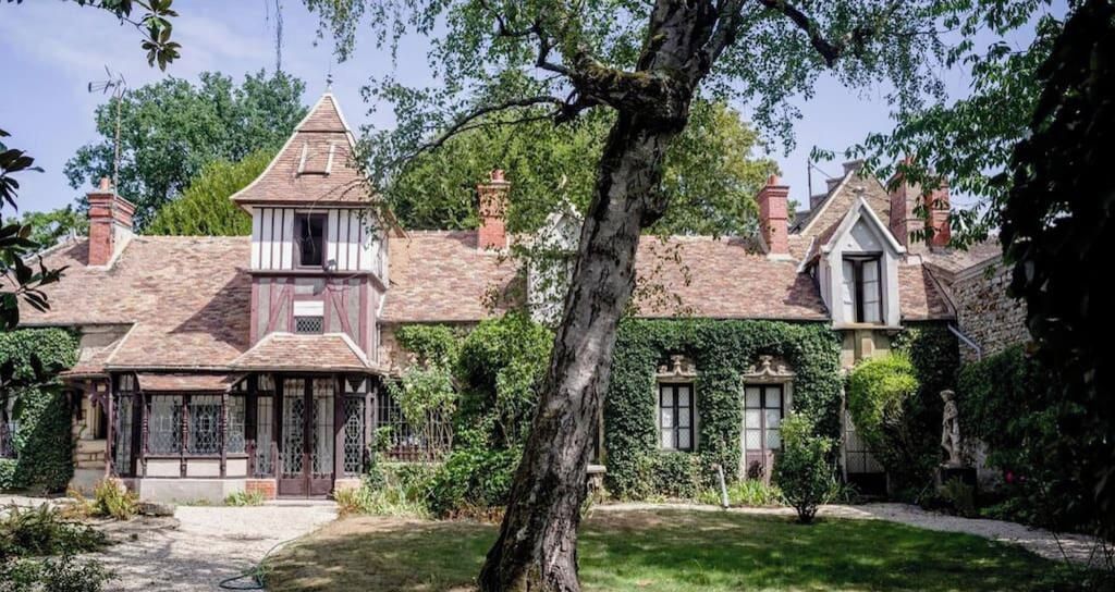 Una casa tradicional con una torre destacada, muros cubiertos de hiedra y un jardín bien cuidado.