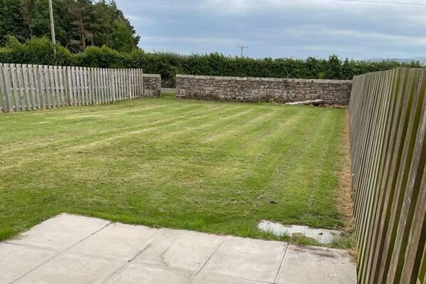 A grassy backyard with a stone wall and a wooden fence. - Cottage - Sleeps 6 - Garden - Parking (Wooler)