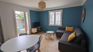 A living room with a sofa, a TV, a dining table, and chairs. There is a window and a door leading to an outdoor area. - Nice little house close to the sea and town center (La Rochelle)
