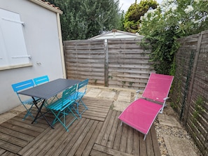 Um pátio com mesa e cadeiras, uma poltrona rosa e um cercado de madeira.