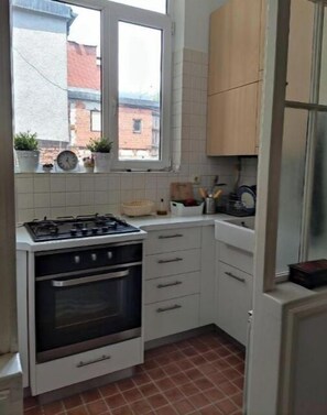 A compact kitchen with white cabinets, a gas stove, an oven, and a window overlooking a brick building.