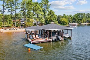 A floating dock with lounge chairs and a covered seating area, surrounded by water and trees.