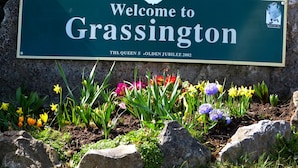 Señal de bienvenida a Grassington, con un letrero de límite de velocidad y flores al frente.