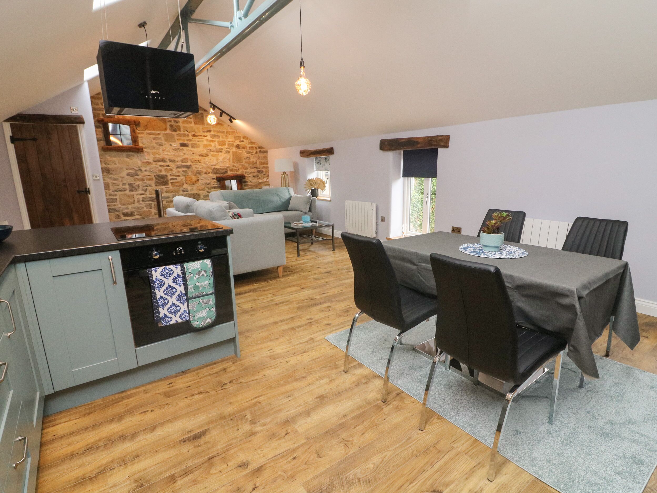 A modern kitchen with a built-in oven, a dining area with a table and chairs, and a living room with a sofa.
