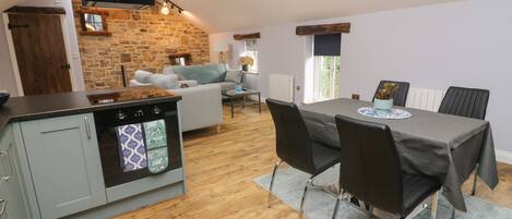 A modern kitchen with a built-in oven, a dining area with a table and chairs, and a living room with a sofa.