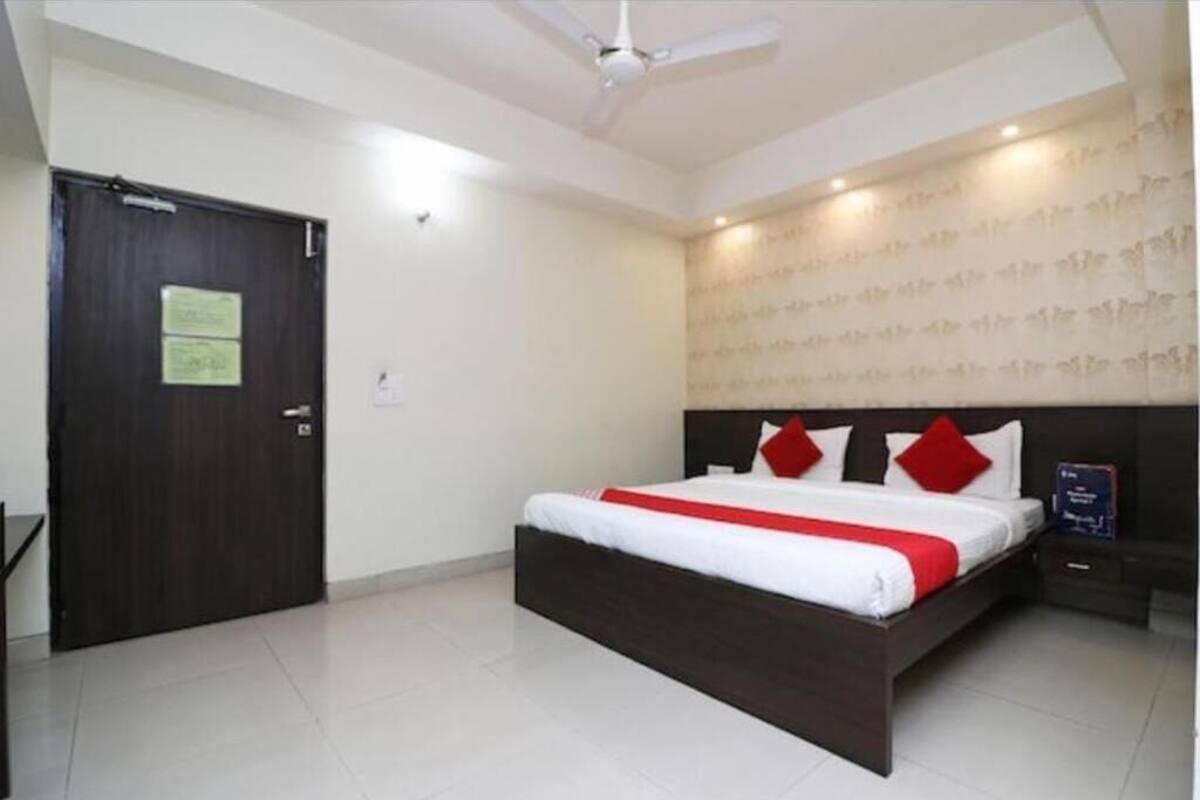 A bedroom with a dark wooden bed, white bedding, and red pillows. There is a ceiling fan, a door with a sign, and a patterned wall.
