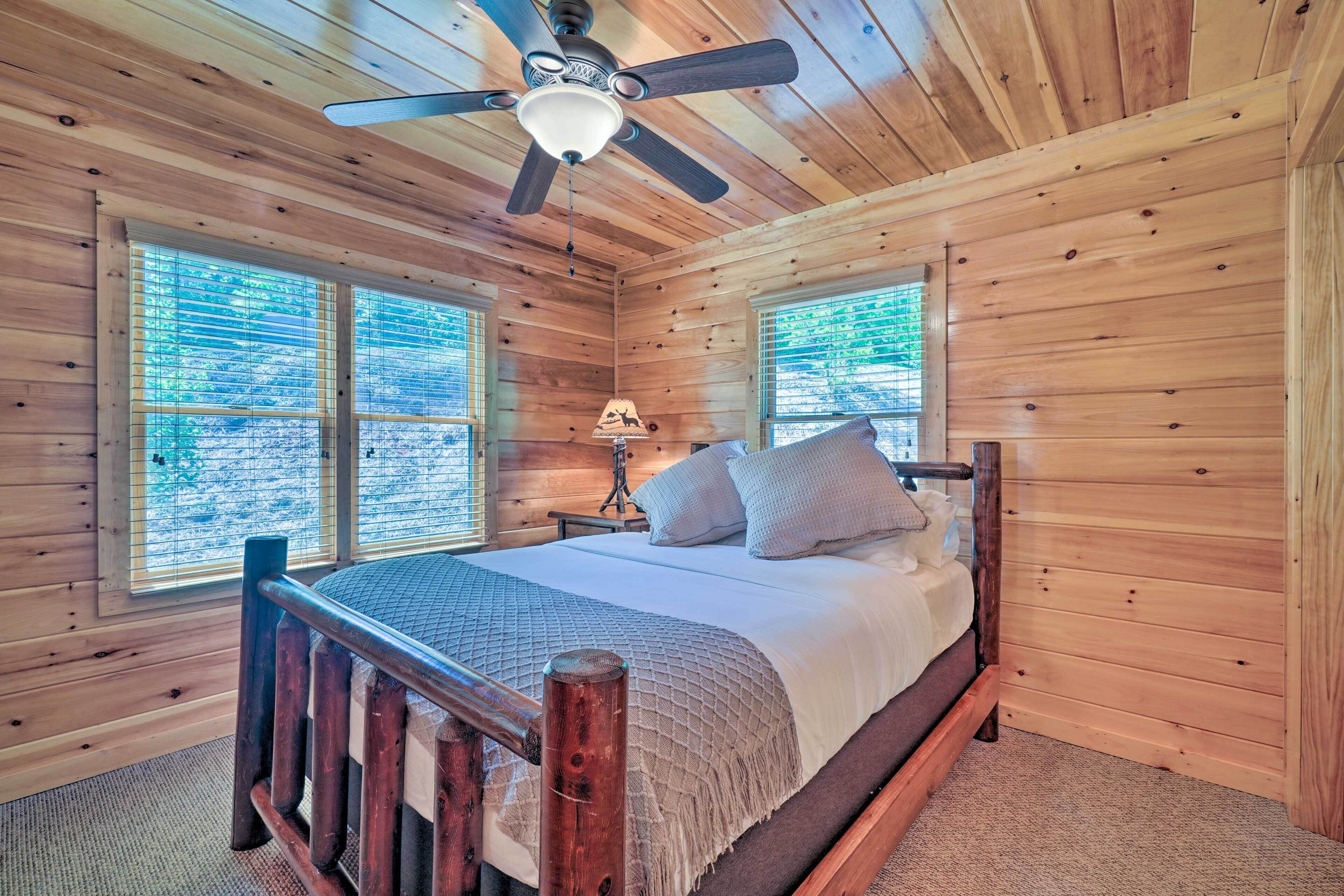 A wooden cabin bedroom with a bed, a nightstand, a lamp, and a ceiling fan.