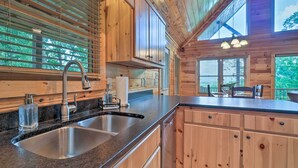 A wooden cabin interior with a kitchen featuring a double sink, wooden cabinets, and large windows allowing natural light. - ‘Hiwassee Hideaway' Cabin w/ Mountain Views! (Murphy)