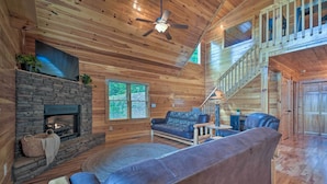 A cozy cabin interior with a stone fireplace, wooden floors, a sofa, and a staircase. - ‘Hiwassee Hideaway' Cabin w/ Mountain Views! (Murphy)
