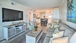 A living room with a TV, sofa, coffee table, and a dining area with chairs and a table. - Myrtle Beach Condo w/ On-Site Pool & Beach Access (Myrtle Beach)