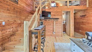 L’intérieur d’un chalet en bois comprend un escalier en bois, un téléviseur, une pancarte de bienvenue et un petit coin cuisine.