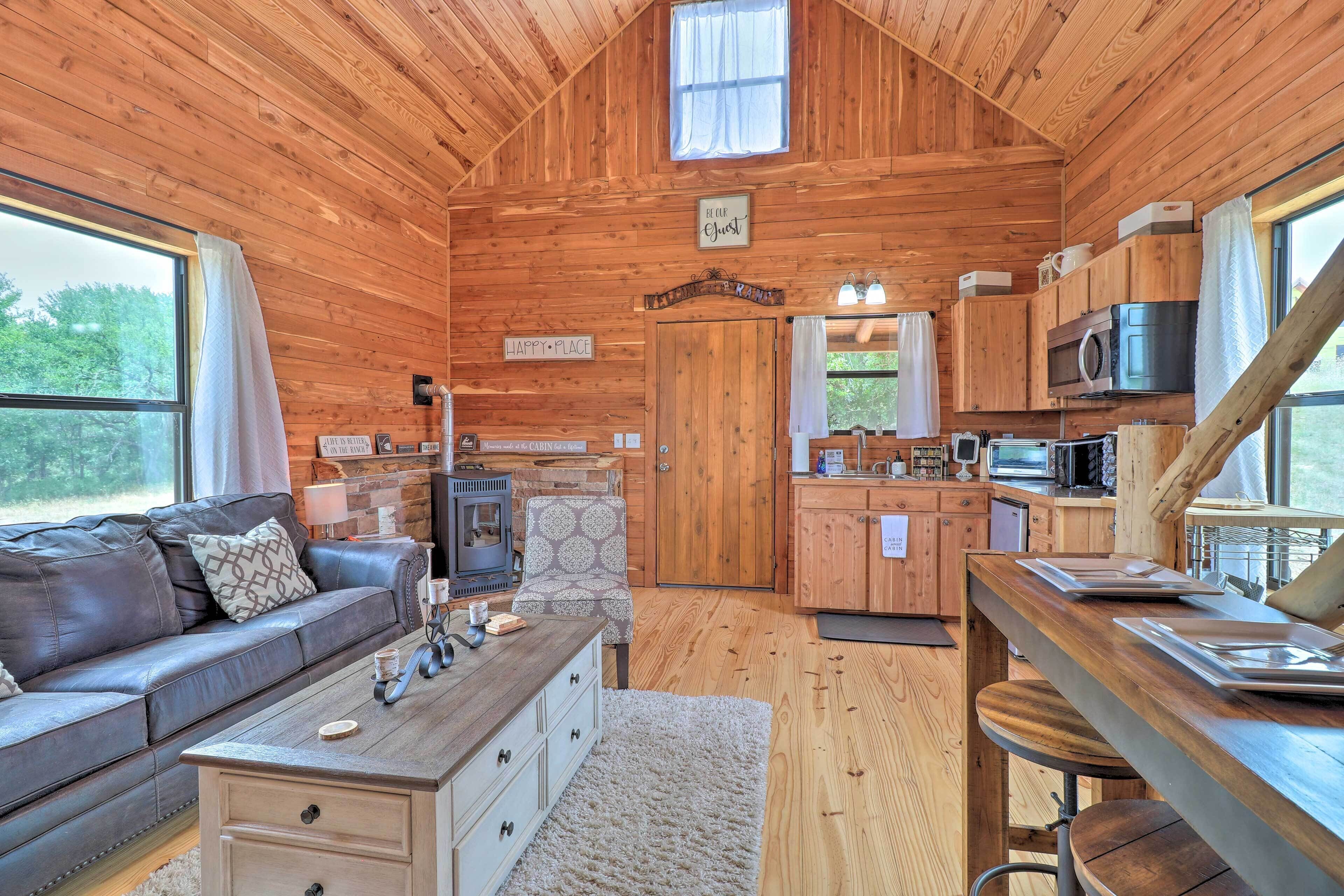 A cozy cabin interior with a wooden interior, a fireplace, a sofa, a dining area, and a kitchen.