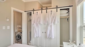 Quarto de hotel com cama, máquina de lavar, armário com roupões e janela.