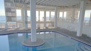 An indoor swimming pool with clear views of the ocean, surrounded by white columns and lounge chairs. - Fontainebleau Terrace by Resort Collection (Panama City Beach)
