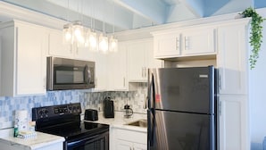 A modern kitchen with white cabinets, a stainless steel refrigerator, a black stove, and a microwave. - Fontainebleau Terrace by Resort Collection (Panama City Beach)