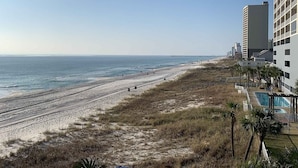 A beach with a long stretch of sand, a pier in the distance, and a tall building with a grid-like facade. - Fontainebleau Terrace by Resort Collection (Panama City Beach)