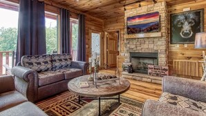 A cozy cabin interior with a stone fireplace, a sofa, a coffee table, and a ceiling fan.