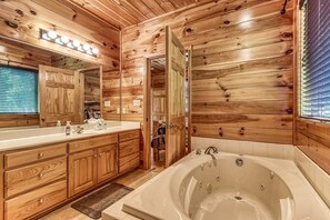 A wooden cabin-style bathroom with a large bathtub, wooden cabinets, and a vanity with a mirror.