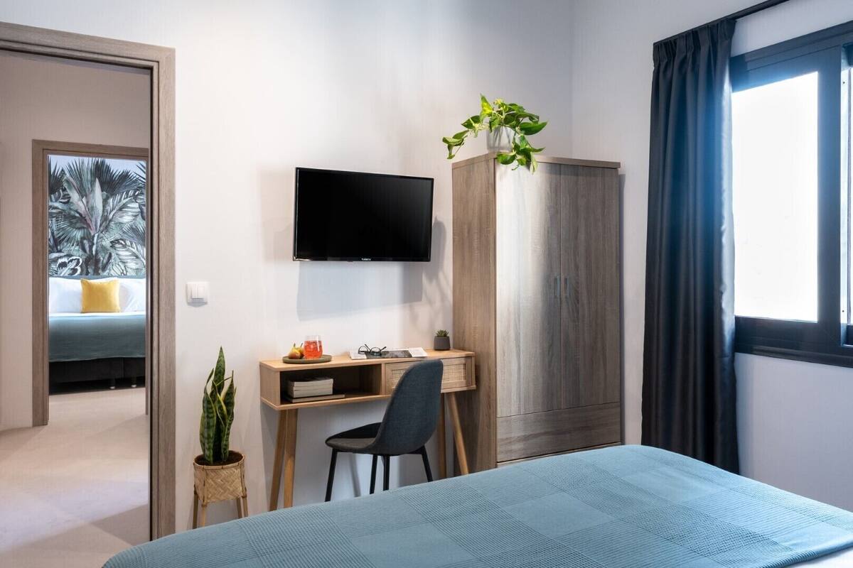 A modern hotel room with a bed, a desk, a TV, and a wardrobe.