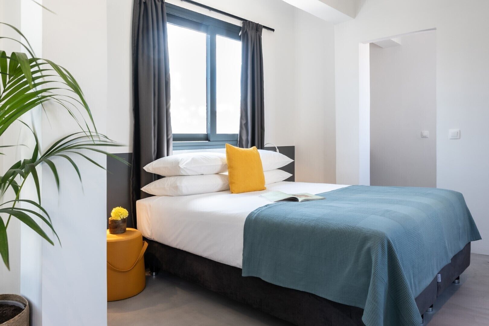 Een moderne slaapkamer met een bed, gordijnen, een potplant en een nachtkastje.
