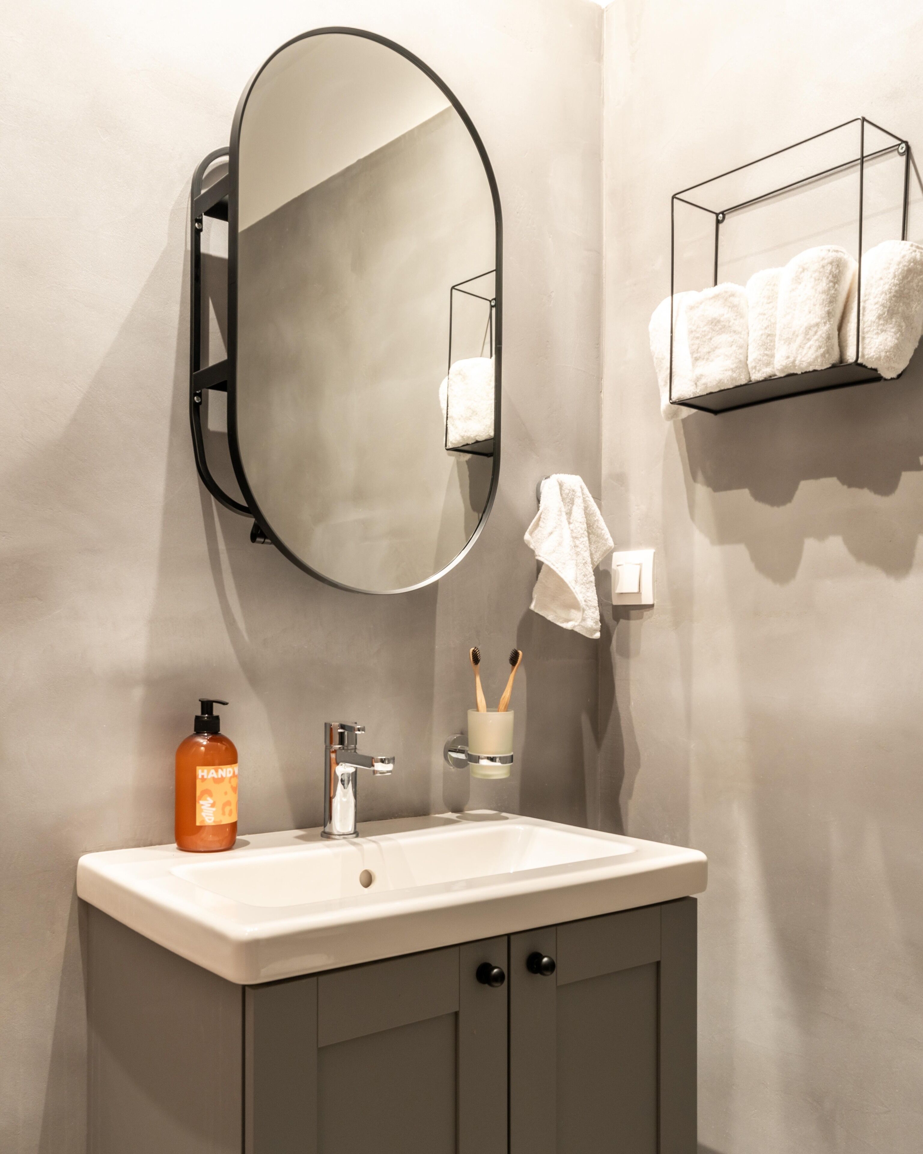 A bathroom with a white sink, a round mirror, a soap dispenser, and a towel rack with two towels.