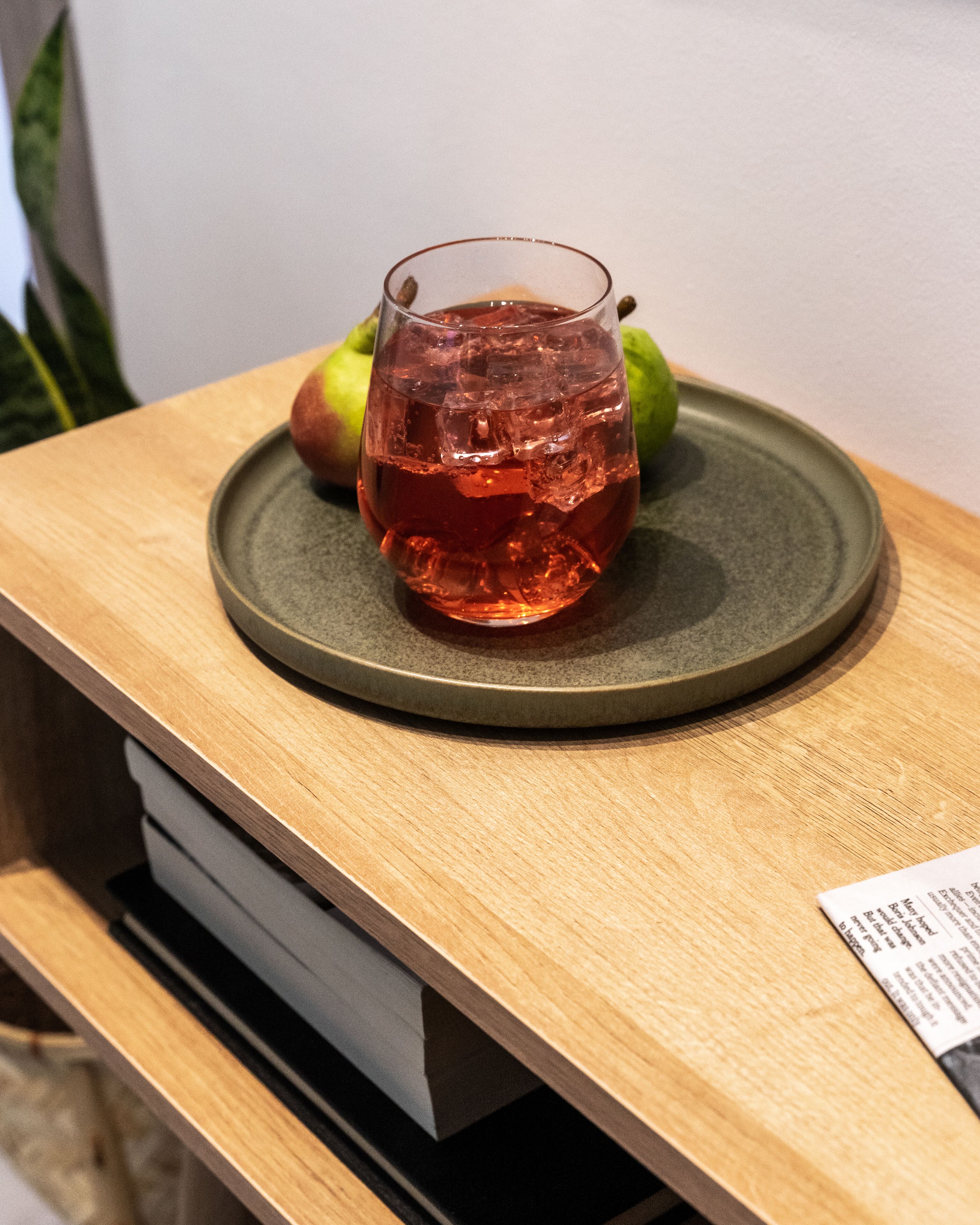 A glass of red beverage on a round ceramic plate on a wooden table.