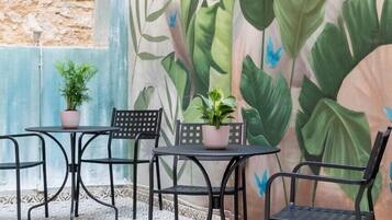 Un patio con mesa y sillas, un mural con follaje tropical y mariposas, y plantas en macetas.