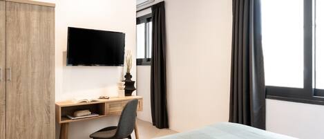 A bedroom with a bed, a desk, a chair, a TV, and a wardrobe.