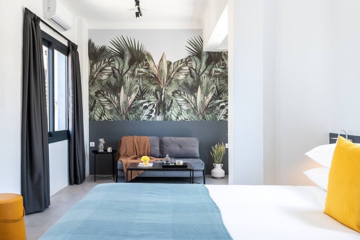 A modern bedroom with a large bed, a sofa, a coffee table, and a tropical leaf mural on the wall.