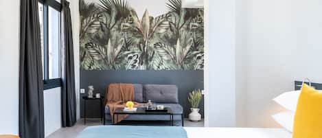 A modern bedroom with a large bed, a sofa, a coffee table, and a tropical leaf mural on the wall.