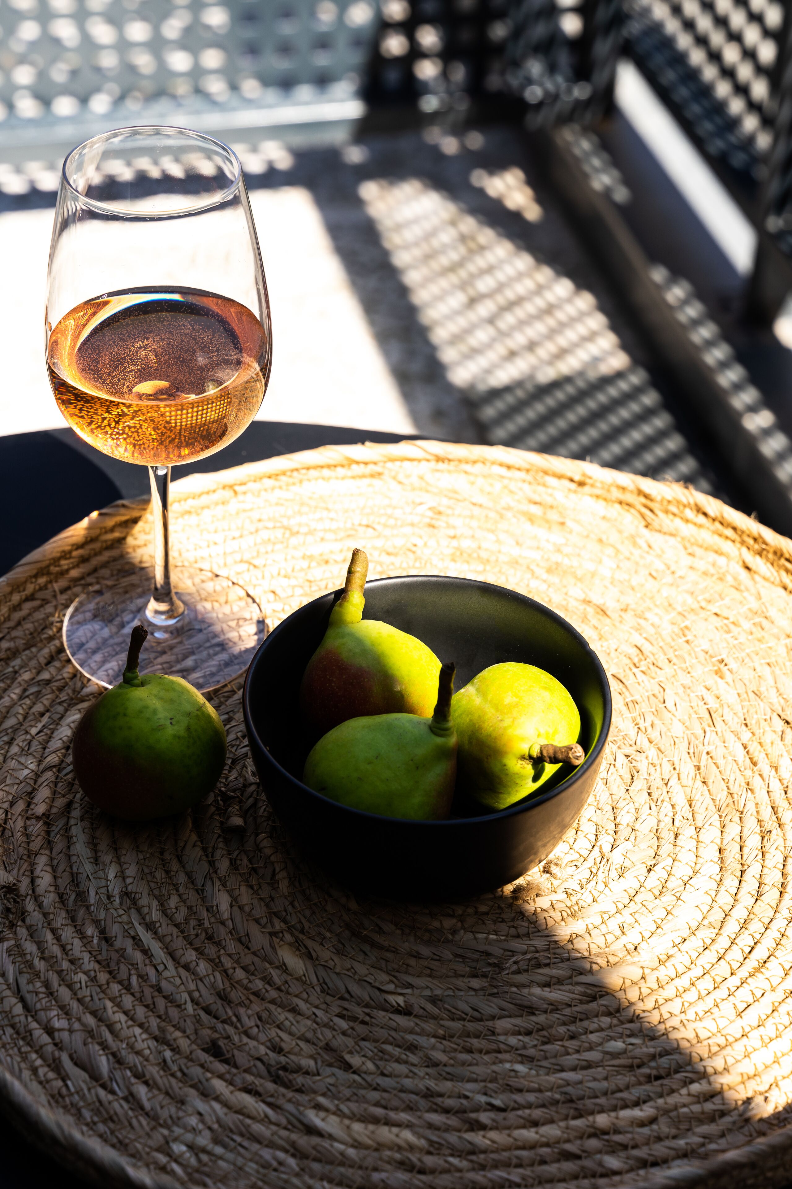 Een glas wijn en een schaal peren op een geweven tafel.