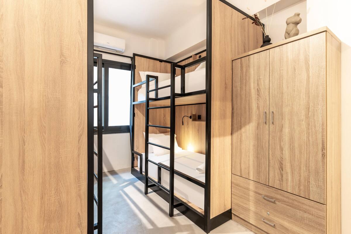 A bedroom with a bunk bed, wooden wardrobe, and a small shelf with decorative items.