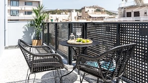 Une terrasse sur le toit avec deux fauteuils en osier, une table ronde sur laquelle se trouve un panier de fruits et une plante en pot.