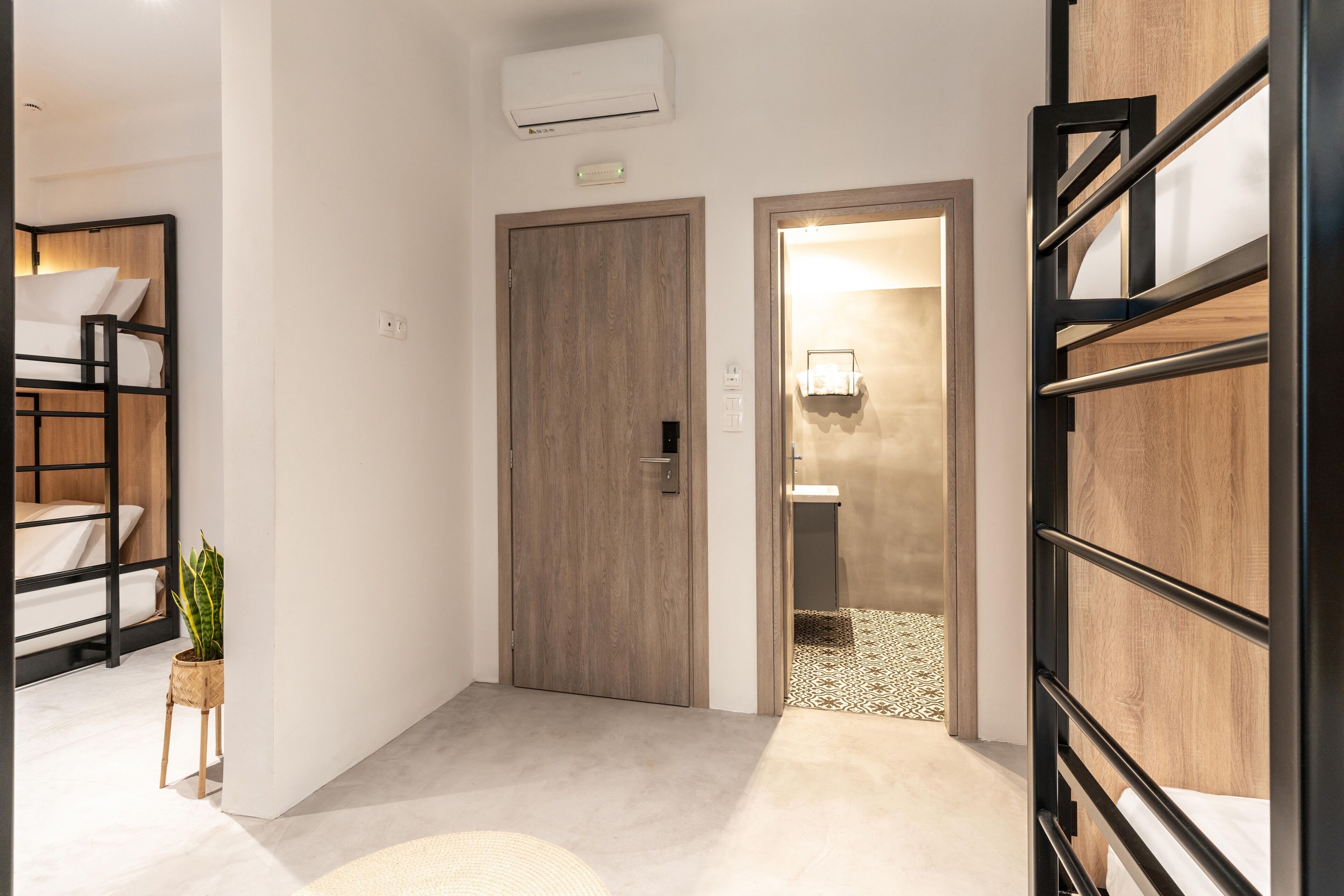 Ein modernes Hotelzimmer mit Etagenbett, einer kleinen Pflanze und einem Badezimmer mit Handtuchhalter.