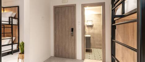 Ein modernes Hotelzimmer mit Etagenbett, einer kleinen Pflanze und einem Badezimmer mit Handtuchhalter.
