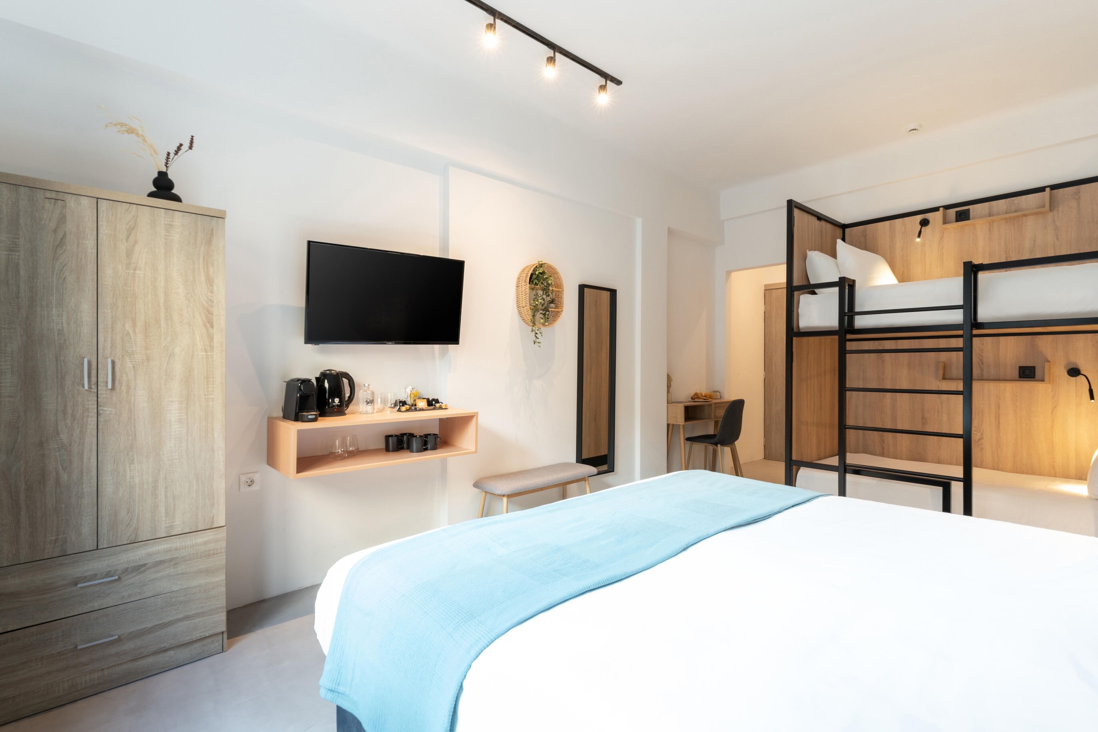 Un dormitorio moderno con una cama litera, un televisor, un armario de madera y una estantería con diversos objetos.
