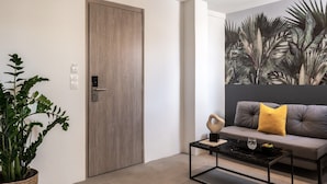 Un salon moderne avec une porte en bois, une grande fresque murale, un canapé gris agrémenté d’un coussin jaune et une table basse noire sur laquelle repose un plateau.