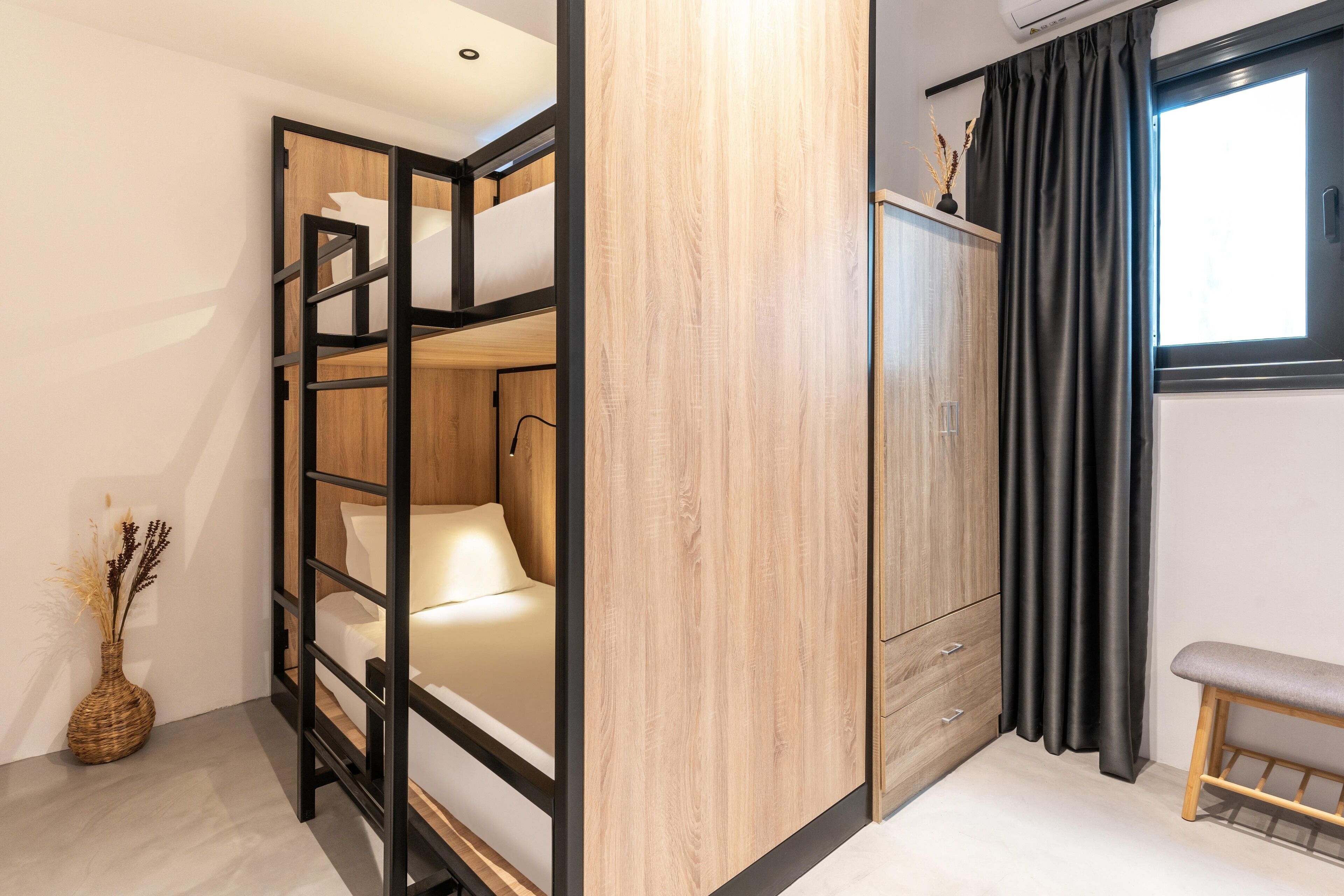 A room with a bunk bed, a wardrobe, a small bench, and a window with curtains.