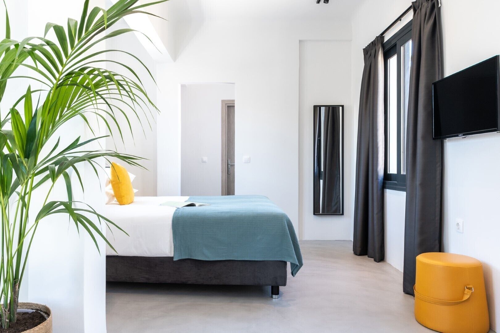 Une chambre à coucher moderne avec un lit, une plante en pot, un téléviseur et une fenêtre avec des rideaux.