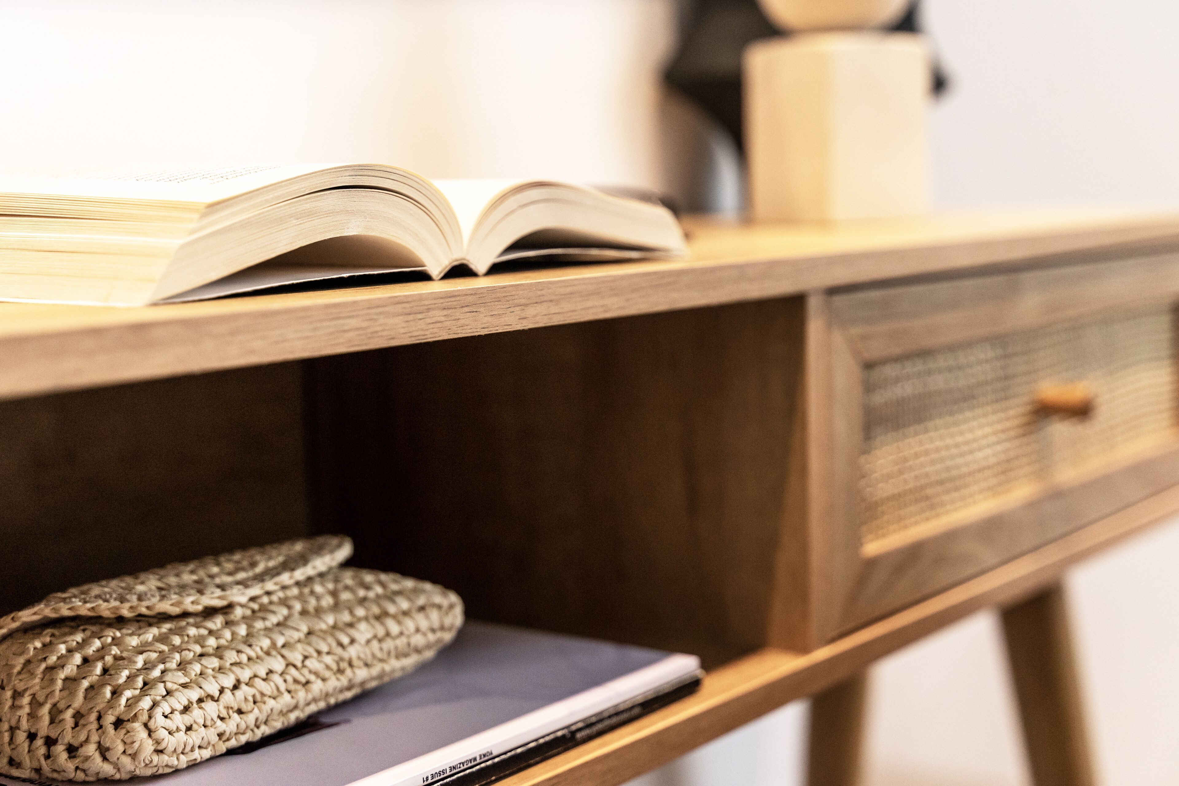Un escritorio de madera con un libro abierto, una computadora portátil y una cesta tejida.