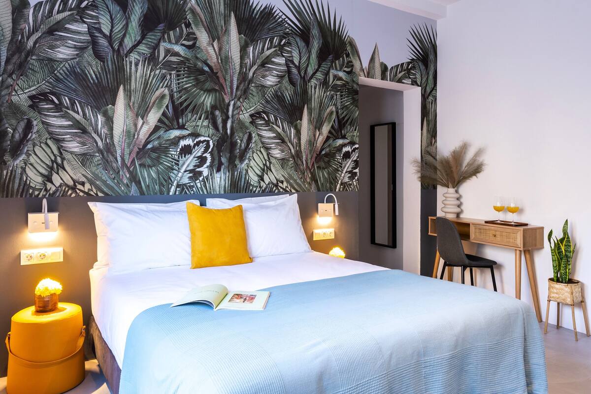 A modern hotel room with a large bed, a desk, and a wall mural.