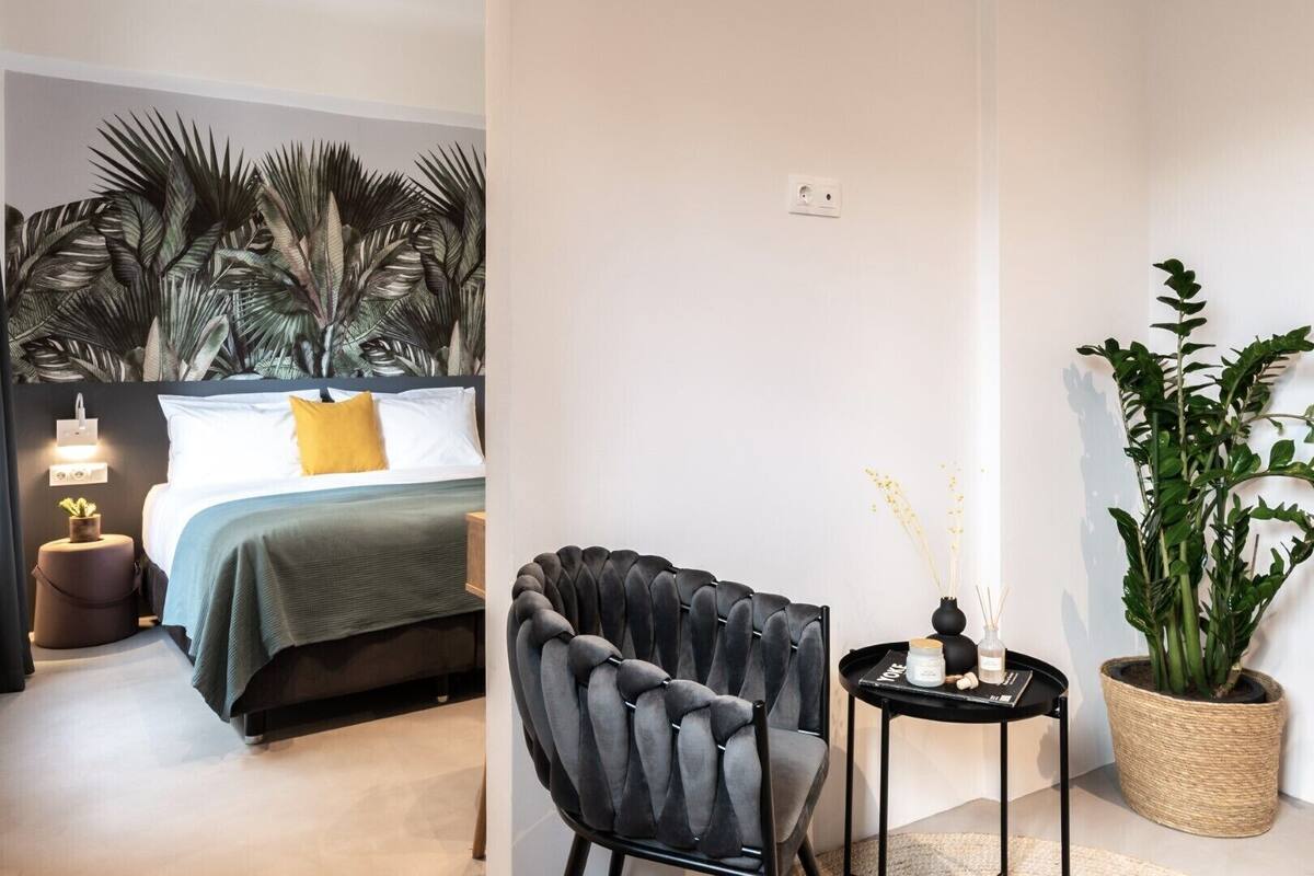 A modern bedroom with a bed, bedside table, lamp, and a potted plant.