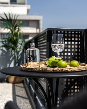 A table with a bottle, a glass, and limes on a woven mat, set outdoors with a building in the background.