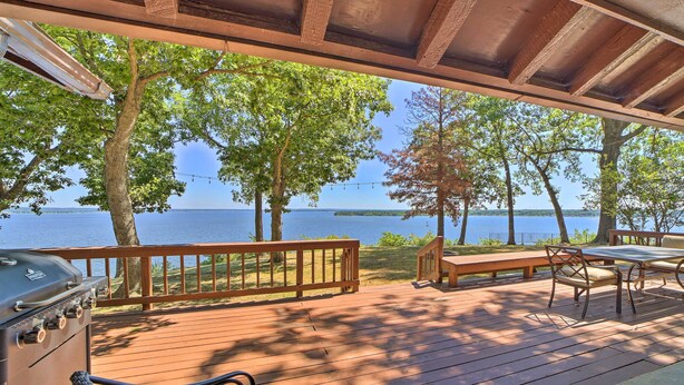Eine Holzterrasse mit Grill, Sitzgelegenheit und Blick auf den See.