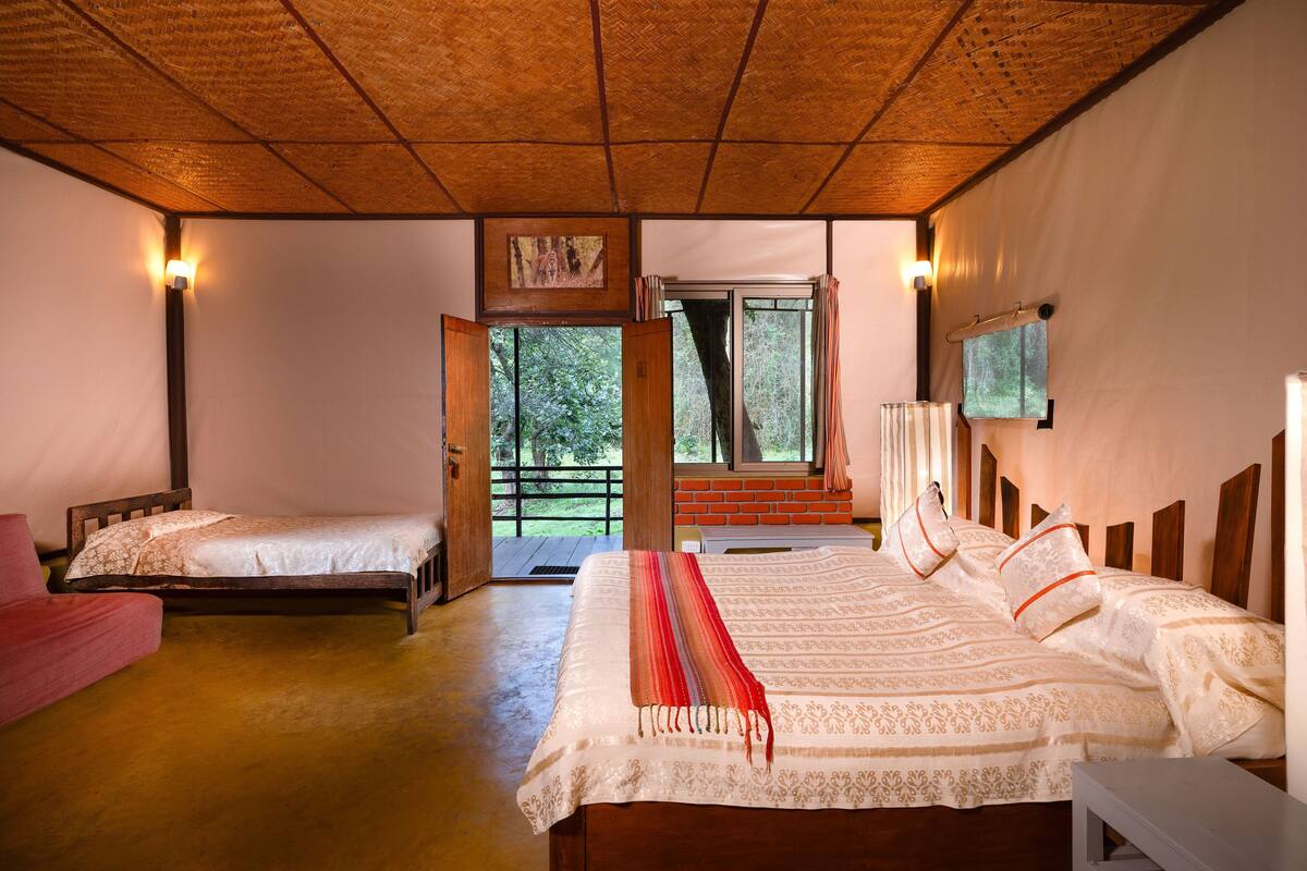 Une chambre avec deux lits simples, un grand lit, un plafond en bois, un téléviseur fixé au mur et une vue sur l’extérieur par une fenêtre.