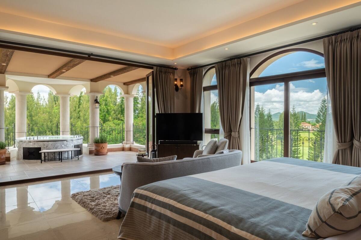 A spacious bedroom with a large bed, a flat-screen TV, and a balcony with a hot tub.