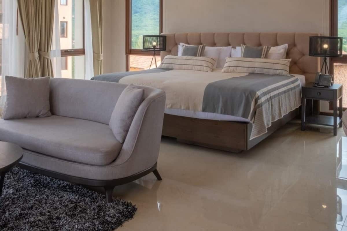 A modern bedroom with a large bed, a sofa, and a nightstand with a lamp.