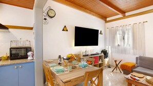 Eine Küche mit Mikrowelle, Toaster und Kaffeemaschine; ein Esstisch mit Stühlen; ein an der Wand befestigter Fernseher und ein Sofa im Wohnbereich.